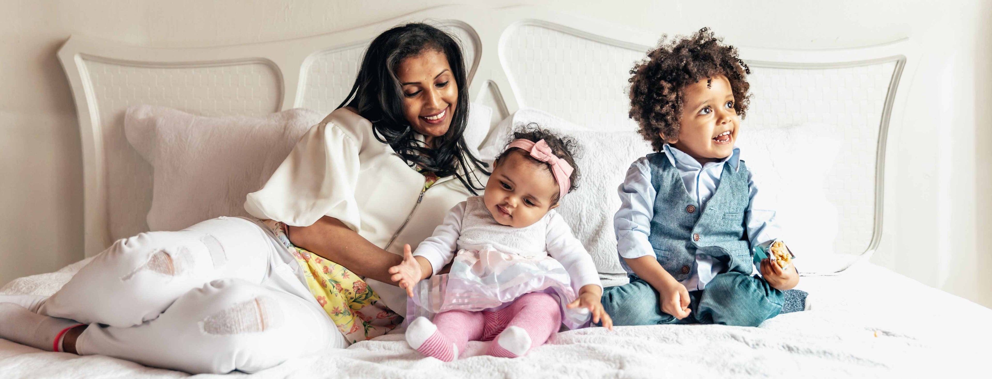 A smiling mother lying on a comfortable and supportive mattress with her happy daughter and smiling son in a beautifully decorated bedroom, showcasing the quality of mattresses from Doms Mattress Store.