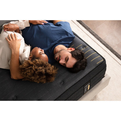 Close-up aerial view of the foot corner of the MLILY ONYX Max Hybrid Plush 14-inch Mattress, man and woman holding each other while asleep, platform base underneath, inside a bedroom with a rug on the floor.