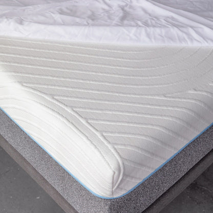 Close up corner view of MLILY Polyester Knit Fabric Mattress Protector on mattress, placed on platform bed frame, mattress protector is only halfway made over the mattress to show that it covers the mattress like a fitted sheet, concrete floor.