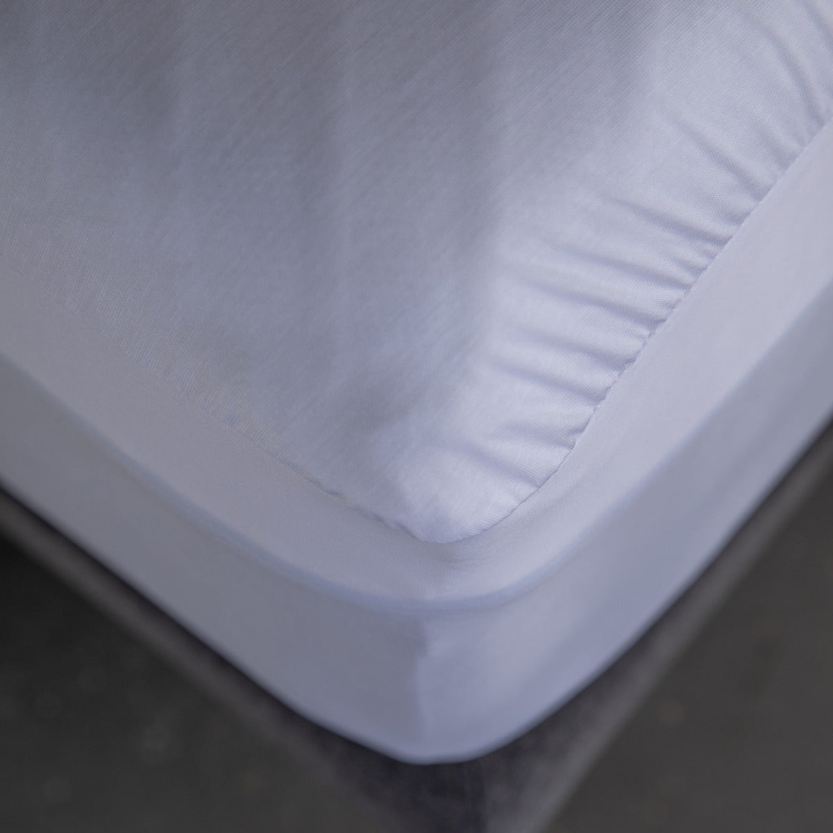 Close up corner view of MLILY Polyester Knit Fabric Mattress Protector on mattress, placed on platform bed frame, mattress protector is over the mattress like a fitted sheet, you can see the details of the material, concrete floor.