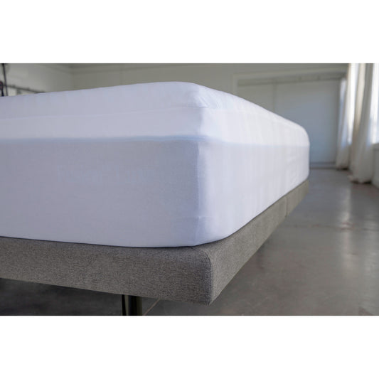 Corner view of mattress on platform bed frame, MLILY Polyester Knit Fabric Mattress Protector covering the mattress like a fitted sheet, inside showroom, concrete floor.