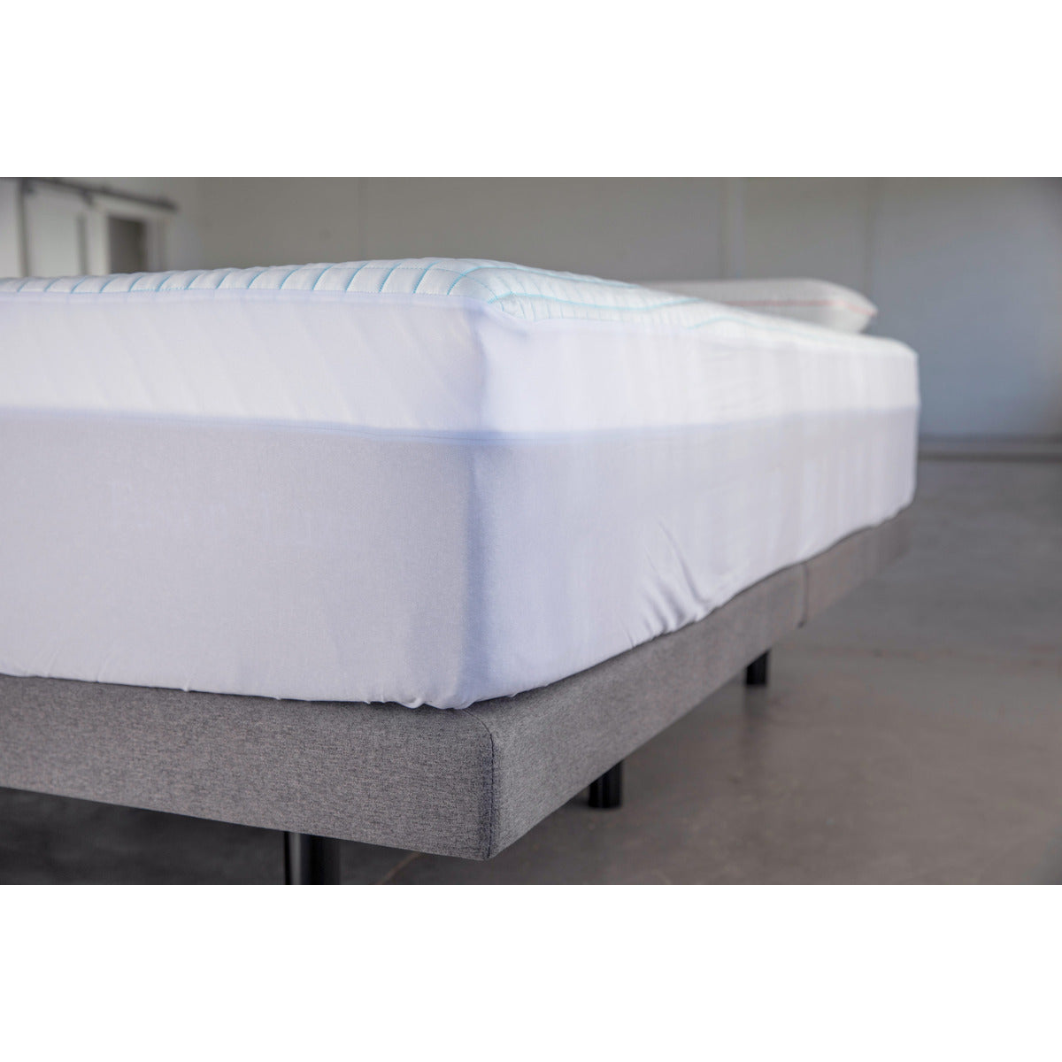 MLILY Cooling Ice Fiber Mattress Protector, shown on a mattress like a fitted sheet, snugly covering the surface inside a warehouse showroom. The protector fits mattresses from 7 to 15 inches thick.