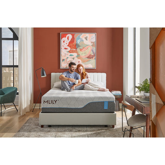 MLILY Harmony Chill 2.0 Memory Foam Medium 14" Mattress on a platform base with a man and woman sitting together, smiling, two pillows at the head of the mattress, inside a decorated bedroom.