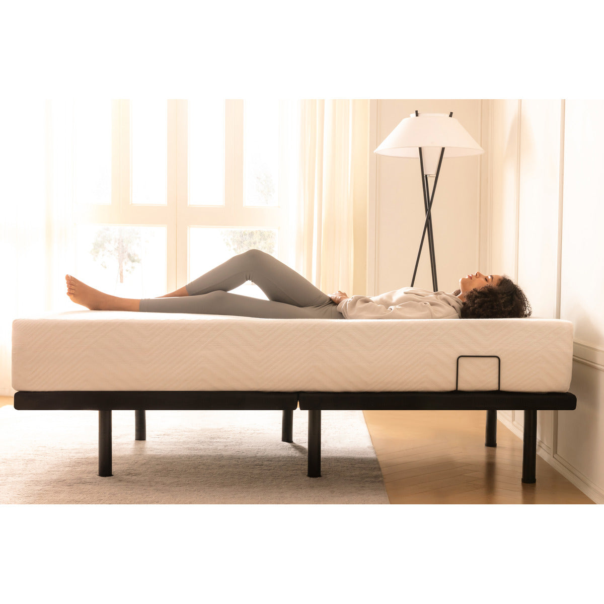 MLILY MS200 Adjustable Base, side view with a mattress on top, a woman sleeping on her back comfortably, the head and foot parts of the adjustable base both in flat position, inside a decorated bedroom.