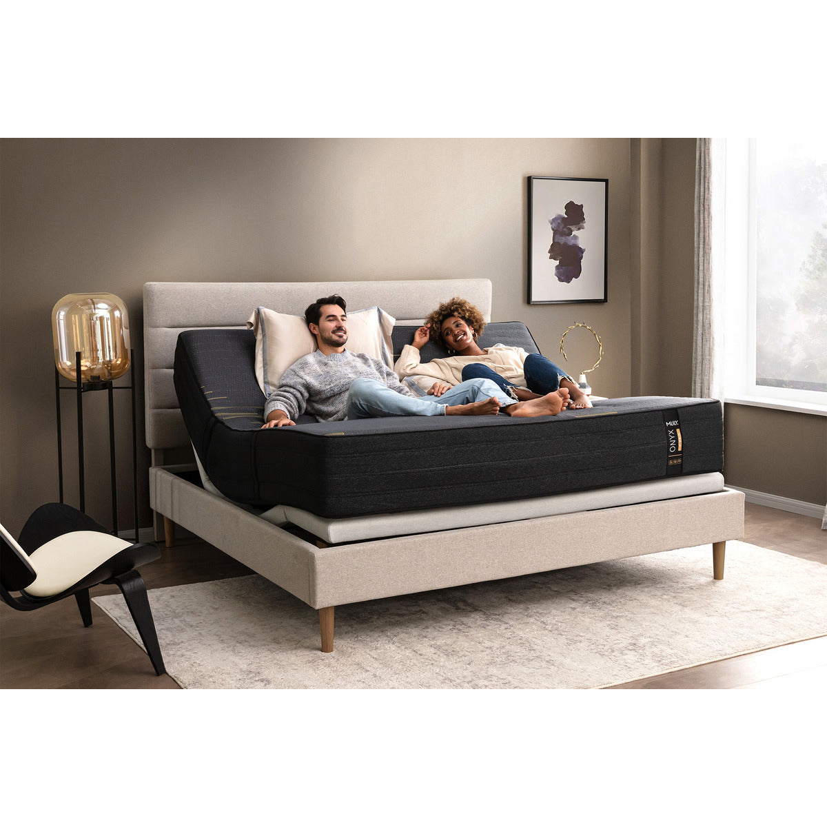 MLILY ONYX Hybrid Firm 12-inch Mattress on adjustable base, slight corner view showing front and side, head and foot raised, man and woman laying on the bed comfortably, smiling, inside a decorated bedroom, man has pillow behind head for additional support.