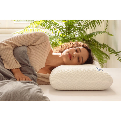 MLILY Serenity Cool Pillow on a mattress, woman sleeping on her right side, contour design fitting neck and shoulders for optimal support, covered with a blanket inside a decorated bedroom.