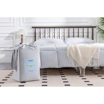 MLILY Soft Washed Down Alternative Comforter in grey, spread across a bed with shams covering two pillows at the head, packaging placed at the corner foot of the bed to compare appearance before and after use, decorated bedroom.