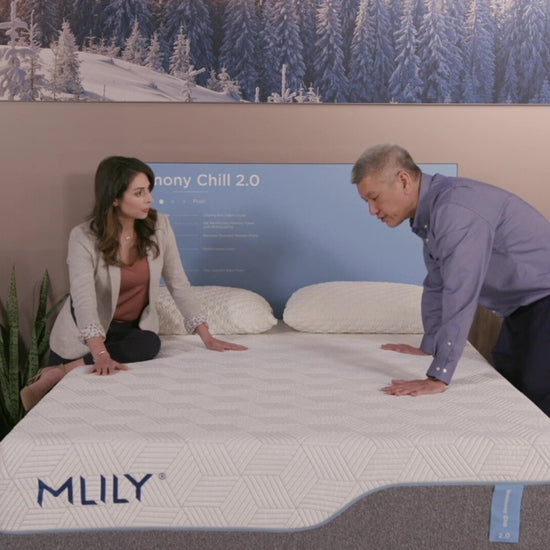 A male sales rep showcases the MLILY Harmony Chill 2.0 Memory Foam Medium 14" Mattress to a woman, highlighting its cooling cover, bamboo charcoal memory foam, breathable layers, performance foam, and PCM coating.