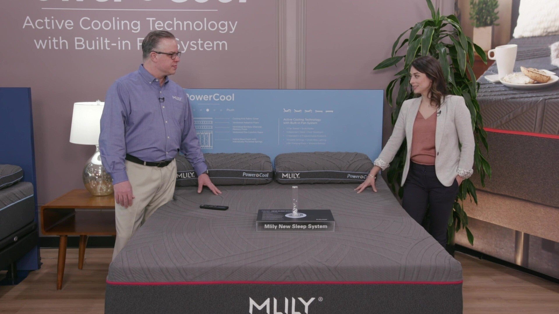 A product specialist explains the MLILY PowerCool Adjustable Base to a woman, highlighting its built-in fans with three speed settings that blow air through the mattress, offering cooling comfort along with full adjustable functionality.