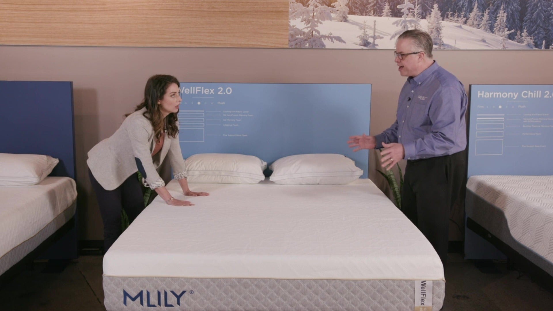 A salesman explains the MLILY WellFlex 2.0 Memory Foam Medium 12" Mattress to a woman, highlighting its medium feel, spine alignment, adaptive foam, cooling gel foam, and ice fabric cover.