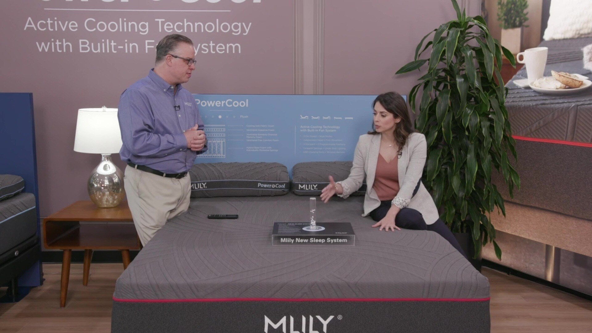 A sales rep explains the MLILY PowerCool Hybrid Medium 11.5" Mattress to a woman, highlighting its plush comfort, hybrid design, cooling knit fabric, ventilated charcoal bamboo memory foam, and airflow system for a cool and supportive sleep.